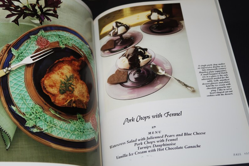 May include: A cookbook page with a photo of a pork chop on a blue and green patterned plate. The text on the page reads "Pork Chops with Fennel" and lists a menu with watercress salad, julienned pears and blue cheese, turnips dauphinoise, and vanilla ice cream with hot chocolate ganache.