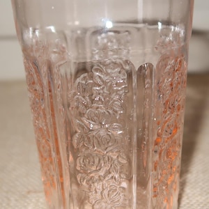 May include: A clear pink glass tumbler with a floral pattern. The glass has a textured surface and is designed for drinking.