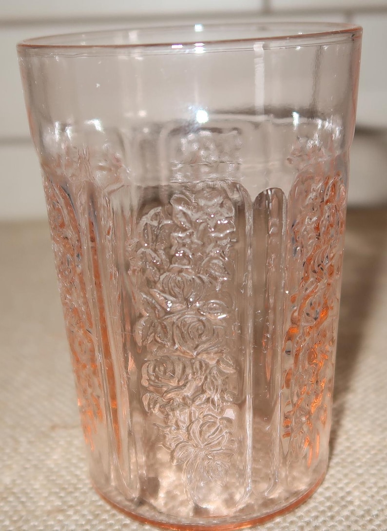 May include: A clear pink glass tumbler with a floral pattern. The glass has a textured surface and is designed for drinking.