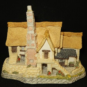 May include: A miniature thatched-roof cottage with a brick chimney, white walls, and a stone base. The cottage has a small door and windows, and a stone path leading to the front door.