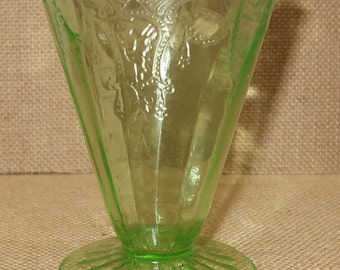 May include: A green glass goblet with a fluted base and a decorative pattern. The goblet is made of Depression glass.