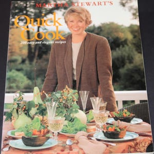 May include: A cookbook titled "Martha Stewart's Quick Cook" with a photo of Martha Stewart on the cover. The book features 200 easy and elegant recipes. The cover also shows a table setting with a floral centerpiece, glasses, and plates.