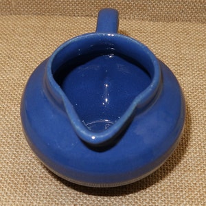 May include: A small, blue ceramic creamer with a handle. The creamer has a smooth, glossy finish.