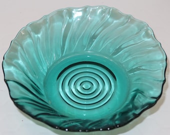 May include: A teal-colored glass bowl with a ruffled edge and a spiral design in the center. The bowl has a circular base and a wavy rim. The glass is transparent, allowing light to pass through.