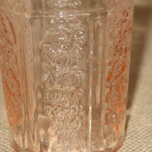May include: A clear, pink glass tumbler with a floral design. The glass has a textured surface and is slightly opaque.