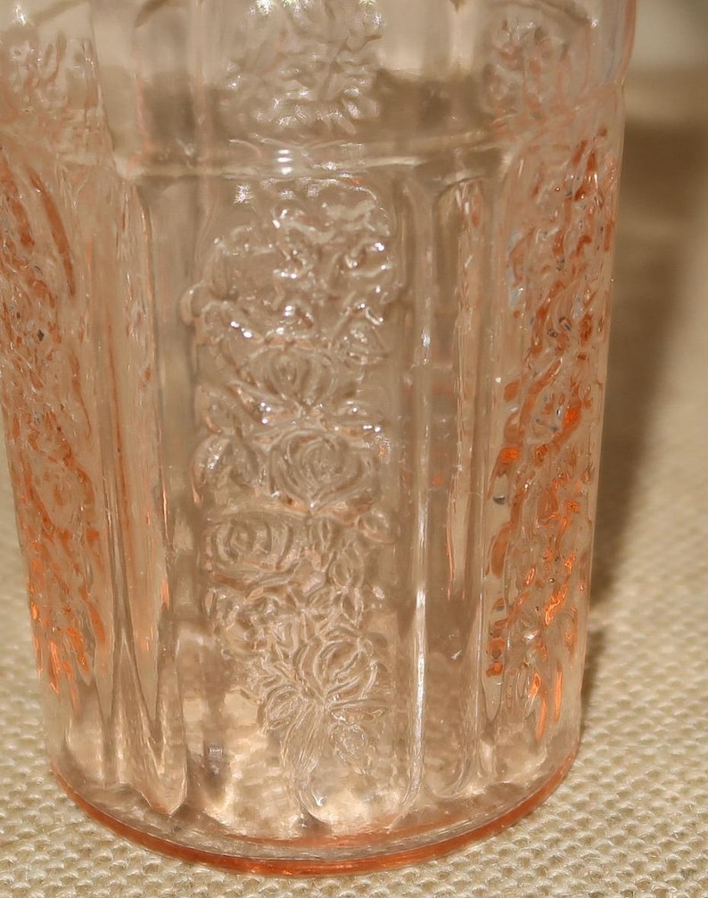 May include: A clear, pink glass tumbler with a floral design. The glass has a textured surface and is slightly opaque.