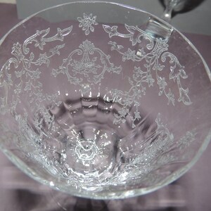 May include: A clear glass goblet with a delicate floral pattern etched into the surface. The goblet has a wide bowl and a tall stem.