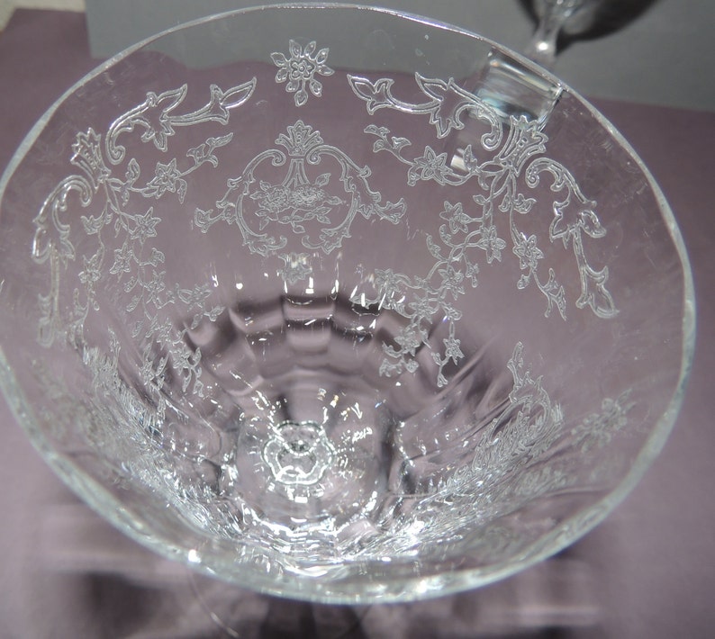 May include: A clear glass goblet with a delicate floral pattern etched into the surface. The goblet has a wide bowl and a tall stem.