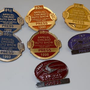 Puede incluir: Una colección de siete pines de prensa de oro y plata para el Salón del Automóvil de Chicago. Los pines son redondos y presentan los años 1989, 1990, 1991, 1993, 1996 y 2000.