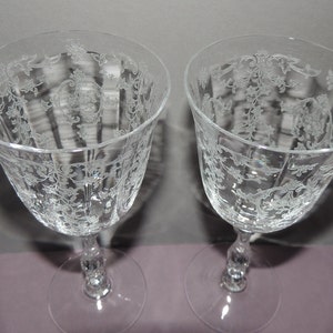 May include: Two clear glass wine glasses with a delicate etched floral pattern. The glasses have a tall, slender stem and a round bowl.