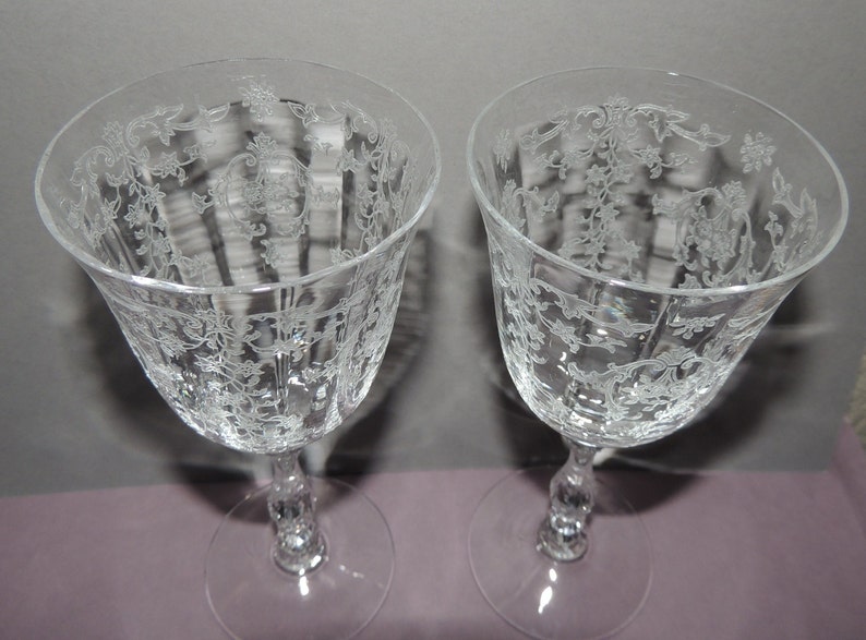 May include: Two clear glass wine glasses with a delicate etched floral pattern. The glasses have a tall, slender stem and a round bowl.