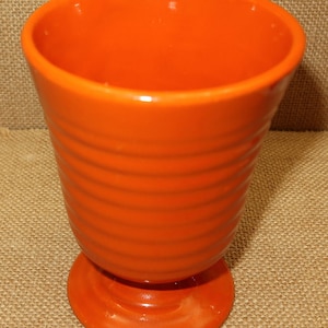 May include: A bright orange ceramic vase with a ribbed design and a footed base.