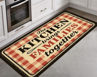 May include: Rectangular kitchen mat with a red and cream checkered pattern and a black border. The mat features the text "The Kitchen brings FAMILIES together" in black and red, with illustrations of a whisk and a spoon.