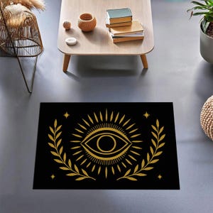 Può includere: Tappeto rettangolare nero con un design a occhio dorato, raggi di sole e foglie di alloro. L'occhio è centrato, circondato da linee radianti e una corona d'alloro. Arredamento per la casa.