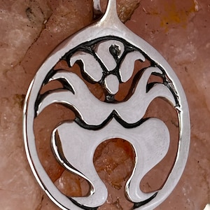 May include: A silver pendant with a circular design featuring a stylized human figure with outstretched arms. The pendant has a loop at the top for attaching to a chain.