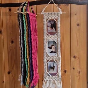 Puede incluir: Dos tapices de macramé colgados de una rama de madera. Uno es una exhibición de fotos con tres marcos. El otro es un colgante de macramé colorido con múltiples hebras en tonos de gris, verde, amarillo, morado y rosa.