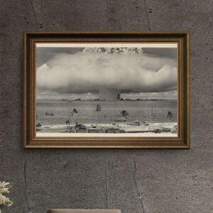 May include: A black and white photograph of a mushroom cloud from a nuclear explosion. The photo is framed in a brown wooden frame.