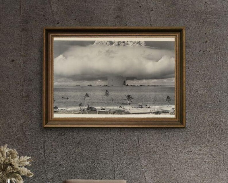 May include: A black and white photograph of a mushroom cloud from a nuclear explosion. The photo is framed in a brown wooden frame.