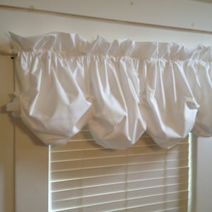 May include: White ruffled window valance with a gathered, poufed design. The valance is made of a lightweight fabric and is hung on a white rod.