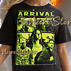 Op de afbeelding: Zwart unisex T-shirt met een filmposterontwerp voor "Arrival" met Amy Adams en Jeremy Renner. Het shirt heeft een ronde hals en korte mouwen. De tekst "Arrival" en "2016" zijn zichtbaar.
