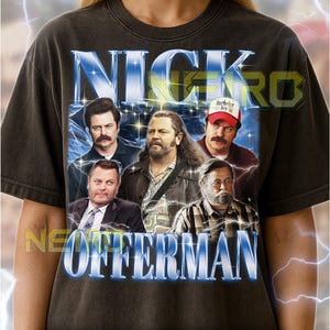 May include: Dark grey unisex t-shirt with a graphic of Nick Offerman and other actors. The shirt has the text "NICK OFFERMAN" in a blue and white design. The shirt is worn by a person.