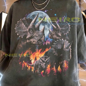 May include: Dark grey unisex t-shirt with a detailed graphic of triceratops dinosaurs, a full moon, and flames. The shirt has a distressed appearance. The text on the shirt reads "NEIRO".