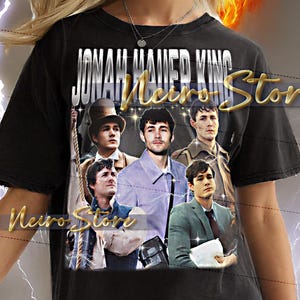 Puede incluir: Camiseta negra con un collage de imágenes y el texto dorado "JONAH MAIER KING Neiro Store". La camiseta la lleva una persona con cabello rubio, con un fondo de diseño llameante y similar a un rayo.
