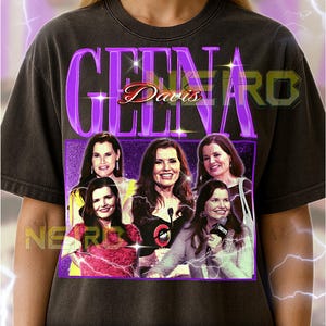 Puede incluir: Camiseta unisex gris oscuro con un diseño gráfico morado con el nombre "Geena Davis" e imágenes de la actriz. La camiseta tiene un estilo vintage con un aspecto desgastado. El texto "NEARB" también es visible.