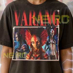 May include: Dark gray unisex t-shirt featuring the word "VARANGO" in red block letters above a framed graphic. The graphic depicts three figures with tribal face paint and headdresses. The shirt has a vintage, worn look.