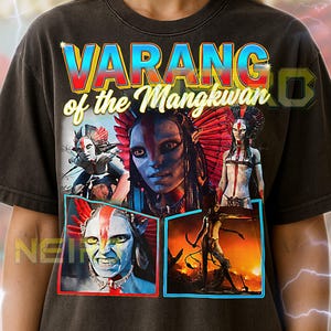 May include: Dark gray unisex t-shirt featuring the text "VARANG of the Mangkwan" in a colorful, retro font. The shirt displays images of characters with blue skin and tribal-inspired attire. The shirt's design includes a red, blue, and yellow color scheme.