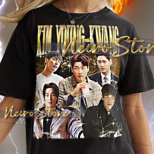 Könnte beinhalten: Schwarzes T-Shirt mit einem goldenen Aufdruck einer Männergruppe und dem Text "KIM YOUNG-KWANG Neiro Store". Das T-Shirt wird von einer Person mit blonden Haaren und Ohrringen getragen.