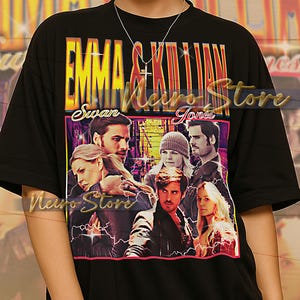 May include: Black t-shirt featuring a colorful graphic of characters from a TV show, with the text "EMMA & KILLIAN" in yellow and red. The shirt has a crew neck and short sleeves. The text "Swan" and "Jones" are also visible.