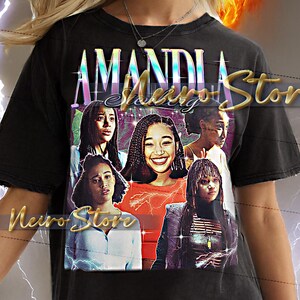 Pode incluir: Camiseta unissex preta com um gráfico de cinco mulheres e o texto "AMANDI" acima e "Neiro Stor" abaixo. A camiseta tem um visual vintage e desgastado. O fundo inclui uma explosão de amarelo e laranja.