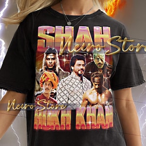 May include: Black unisex t-shirt featuring a graphic design with the text "SHAH Neuro Store" and "SHAH RUKH KHAN". The design includes images of several people. The model is wearing a 2XL shirt.