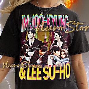 May include: Black t-shirt featuring a graphic design with the text "IM JOO-KYUNG & LEE SU-HO" in yellow and white. The design includes images of people. The model is wearing the shirt.