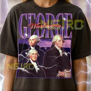 Peut inclure: T-shirt gris foncé avec un motif de George Washington et le texte "GEORGE Washington" en violet et rouge. Le t-shirt a un aspect vintage et vieilli.
