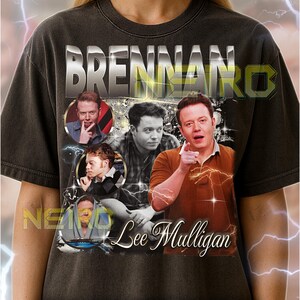 May include: Dark gray unisex t-shirt featuring a graphic of Lee Mulligan with the text "BRENNAKO" above and "Lee Mulligan" below. The shirt includes multiple images of Lee Mulligan. The text on the shirt says, "The first model is wearing a XL shirt."