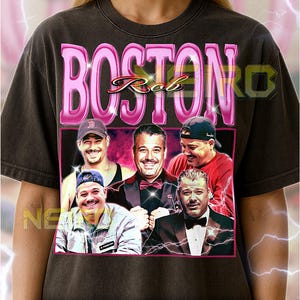 Puede incluir: Camiseta unisex gris oscuro con un gráfico de cinco hombres y el texto rosa "BOSTON Rob". La camiseta incluye el texto: "El primer modelo lleva una camiseta XL. Esta camiseta unisex es fiel a la talla. Para un look oversize, selecciona 1 o 2 tallas más grandes de lo habitual."