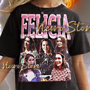 Puede incluir: Camiseta unisex negra con el nombre "FELICIA" en letras rosas y doradas. La camiseta tiene un gráfico de múltiples imágenes de una mujer. La camiseta es de estilo unisex.