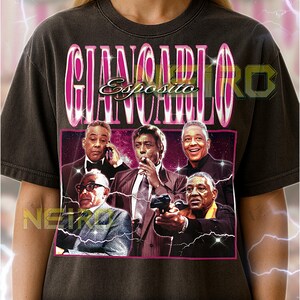 Könnte beinhalten: Dunkelgraues Unisex-T-Shirt mit einer Grafik von Giancarlo Esposito und dem Text "GIANCARLO ESPOSITO" in einem rosa-weißen Design. Die Grafik enthält mehrere Bilder des Schauspielers. Das Shirt hat einen Vintage-Stil.