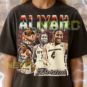 May include: Dark gray unisex t-shirt featuring the name "ALIYAH" in a retro style. The shirt includes images of a basketball player and the word "Boston". The shirt also has the text "FEVER" and "SOUTH CAROLINA".