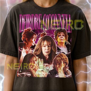 Puede incluir: Camiseta unisex gris oscuro con un gráfico rosa con el nombre "DEIRDRE O'CONNELL" y un collage de imágenes. El texto "NEIRO" también es visible. La camiseta es fiel a la talla.