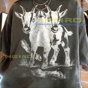 May include: Dark gray unisex t-shirt featuring a white illustration of a two-headed goat. The graphic is detailed with shading and texture. The shirt has short sleeves and a crew neck. The text "NEIRO" is visible on the shirt. The shirt fits true to size.