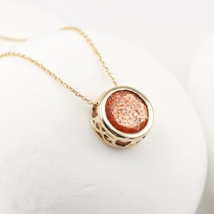 May include: A gold necklace with a round pendant featuring a sunstone gemstone. The pendant has a delicate, openwork design.