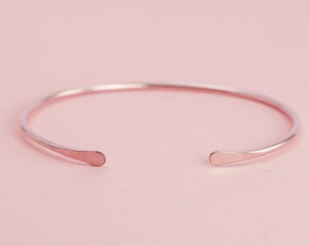 May include: A simple, minimalist rose gold bangle bracelet with a smooth, rounded finish.