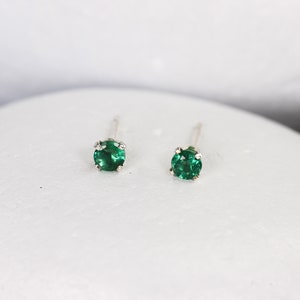 Puede incluir: Un par de pequeños pendientes de botón redondos de color verde esmeralda con engastes de plata.