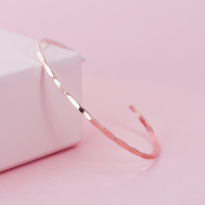 Pode incluir: Um bracelete delicado de ouro rosa martelado. O bracelete &eacute; fino e tem um design simples e minimalista.