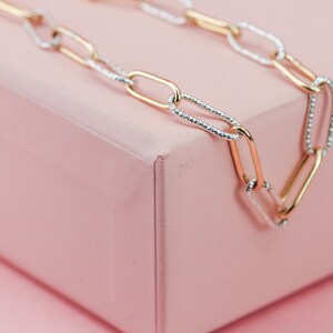 May include: A gold and silver chain necklace with a textured design. The chain is made of interlocking oval links.