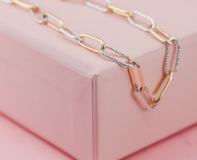May include: A gold and silver chain necklace with a textured design. The chain is made of interlocking oval links.