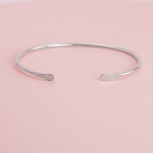 May include: A simple silver bangle bracelet with rounded ends. The bracelet is open and ready to be worn.